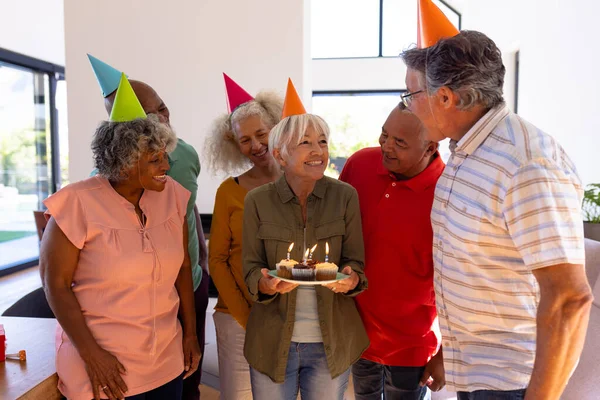 Amigos Multirraciales Mirando Mujer Mayor Emocionada Sosteniendo Cupcakes Cumpleaños Casa —  Fotos de Stock