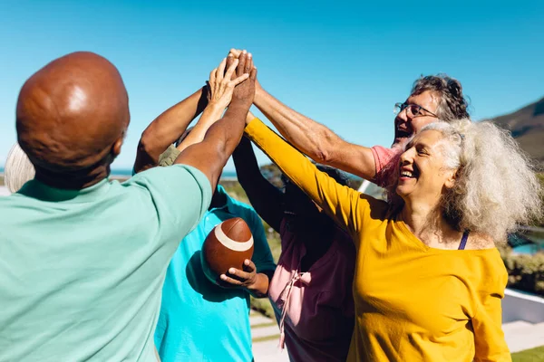 stock image Multiracial seniors giving high-five while playing rugby against clear sky in yard at nursing home. Summer, friends, unaltered, sport, togetherness, enjoyment, support, assisted living, retirement.