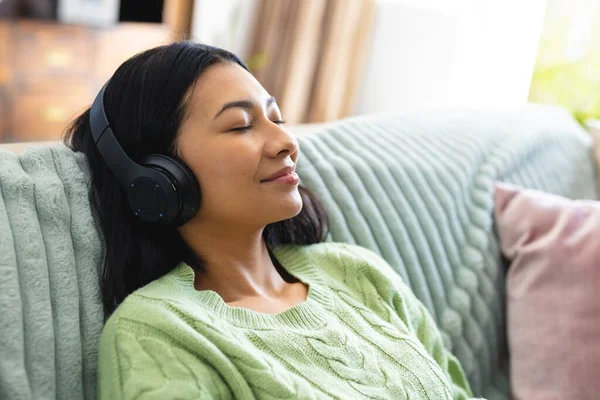 Obraz Szczęśliwej Birasowej Kobiety Słuchawkach Relaksującej Się Sofie Zamkniętymi Oczami — Zdjęcie stockowe