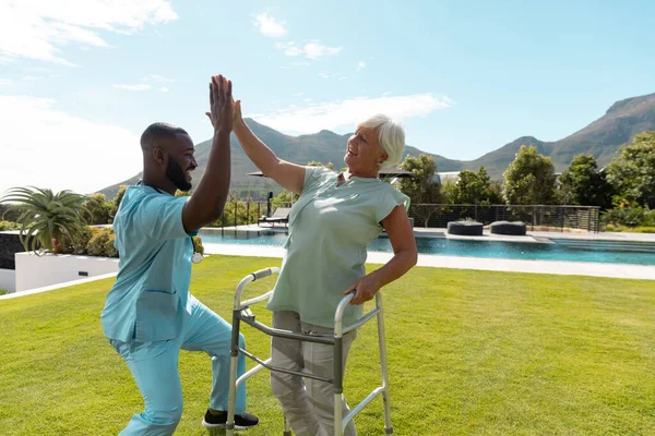 アフリカ系アメリカ人男性の健康労働者と白人のシニア女性が庭で互いに高い5分の1 医療と定年退職シニアライフスタイルの概念 — ストック写真