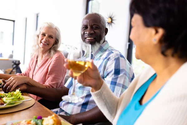 在养老院 多种族的老年夫妇牵着手 而妇女则在餐桌边品酒 不变的爱 辅助生活和退休 — 图库照片