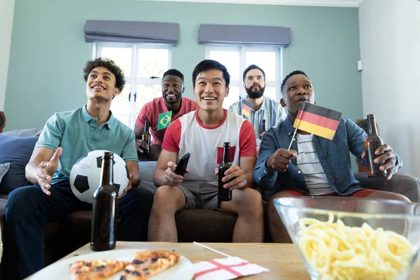 多种族好奇的男性朋友 家里有啤酒瓶 旗帜和看足球比赛的球 社交活动 周末活动 — 图库照片