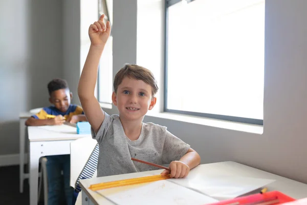 教室の机に腰掛けて手を上げて笑顔の白人小学生 変化のない教育子供時代学習学校の概念 — ストック写真