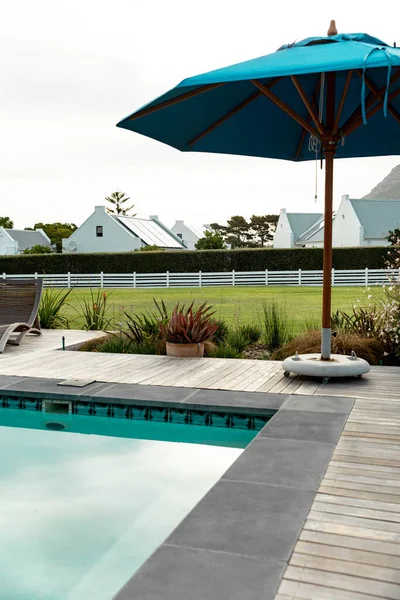 プールサイドの青い傘と緑豊かな庭 屋上に太陽光パネルのある家 コピースペース 太陽エネルギー 緑の技術と持続可能性の概念 — ストック写真