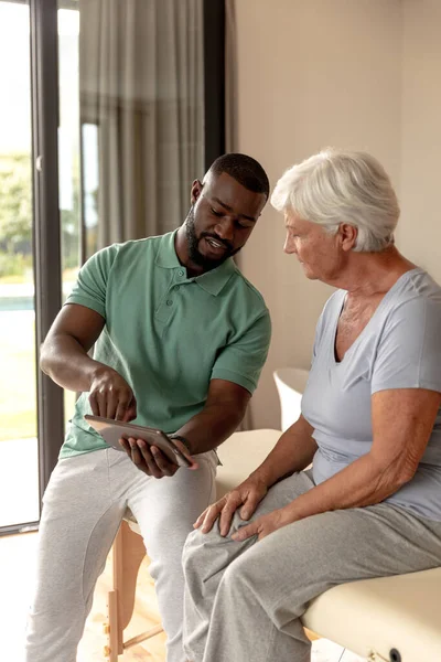 Afrykański Amerykański Fizjoterapeuta Pokazuje Tabletki Cyfrowe Białej Seniorce Domu — Zdjęcie stockowe