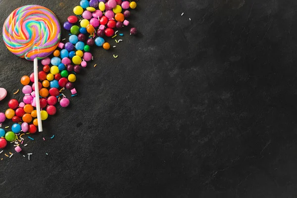 ブラックテーブルの上に複数の色のチョコレートキャンディーと渦巻ロリポップの直接上記のビュー 変化のない不健康な食生活と甘い食の概念 — ストック写真