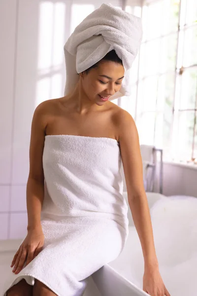 Vertical Happy Biracial Woman Wearing Towel Sitting Edge Bath Smiling — Stock Photo, Image