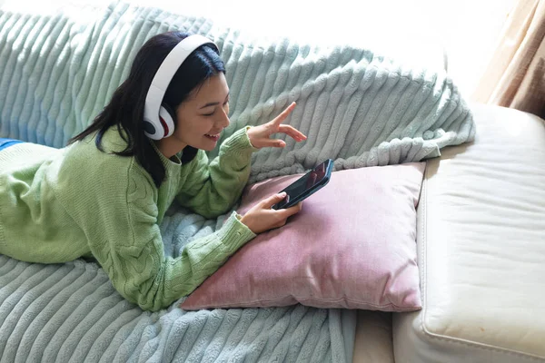 照片中快乐的女人在耳机里用智能手机躺在沙发上 复制空间 技术和家庭生活概念 — 图库照片