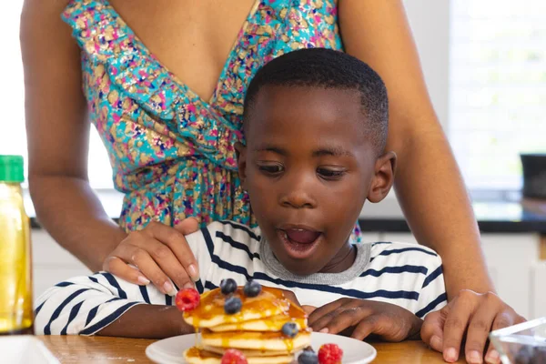 口を開けてパンケーキや果物を見て 息子のそばに立つ多人種間の母親の中央部 変更されていない 一緒に 子供時代 食べ物 ライフスタイルと家庭の概念 — ストック写真