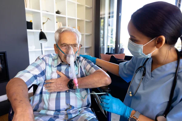 分娩时的女性保健工作者帮助高加索老年人在家里使用氧气面罩 医疗和退休老年人生活方式概念 — 图库照片