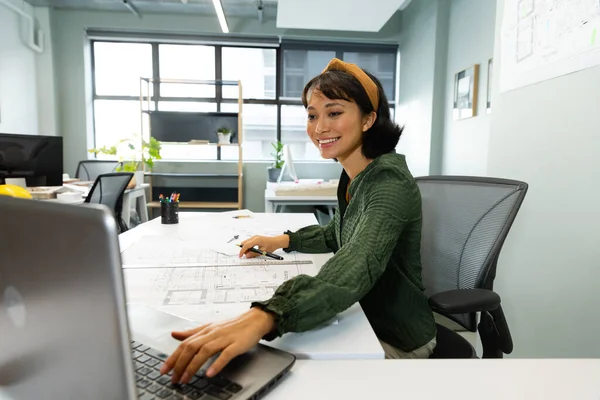 オフィスのテーブルでラップトップを使用して青写真と笑顔アジアの若い女性建築家 変更されていない 創造的なビジネス デザインの専門家 フロアプラン — ストック写真