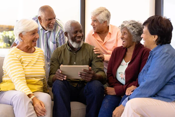 多种族老年人拿着数码平板电脑 坐在沙发上看着笑着的朋友 疗养院 无线技术 未经改动 辅助生活 — 图库照片