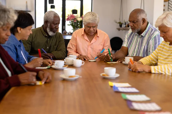 多种族男性和女性高级朋友与咖啡和饼干在饭桌上玩宾果 疗养院 休闲游戏 辅助生活 — 图库照片