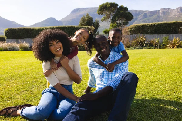 在院子里的草地上 快乐的多种族孩子从后面拥抱着父母的肖像 不变的家庭 夏天和自然的概念 — 图库照片