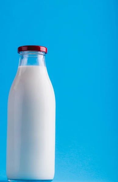 Close-up of milk in glass bottle against blue background, copy space. unaltered, food, drink, studio shot and healthy food concept.