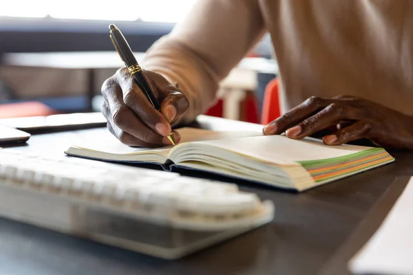 アフリカ系アメリカ人の成熟した実業家が事務所のデスクで日記を書いている 変化のない創造的なビジネス職場職業 — ストック写真