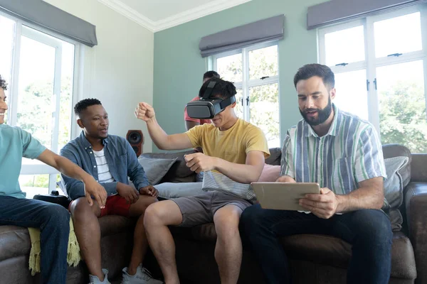 多种族男子穿着虚拟现实模拟器的手势和朋友使用数字Pc在沙发上 未来主义 享受和周末活动概念 — 图库照片