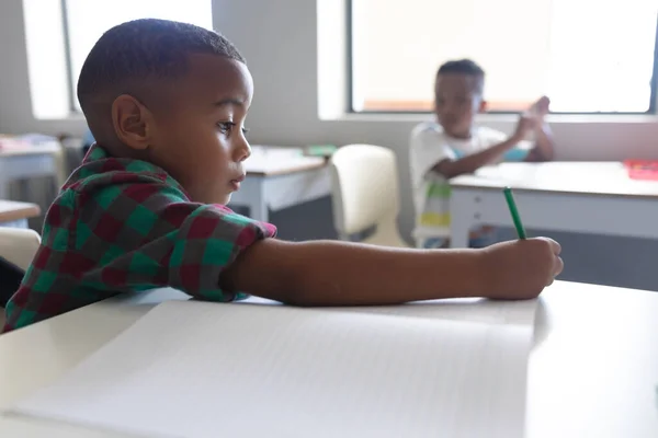 アフリカ系アメリカ人の小学生が教室の机で本を書いている 変化のない教育子供時代学習学校の概念 — ストック写真