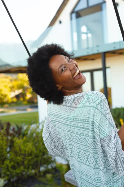 庭でスイングにスイングしながら笑顔アフリカ系アメリカ人女性の肖像画 旅行と休暇のコンセプト — ストック写真
