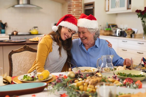 Vanhempi Valkoihoinen Nainen Hänen Aikuinen Tyttärensä Istuvat Päivällispöydässä Yhdessä Jouluhatut — kuvapankkivalokuva