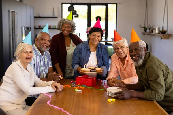 多种族快乐的老朋友戴着派对帽 女人拿着纸杯蛋糕的画像 辅助生活和退休之家 — 图库照片
