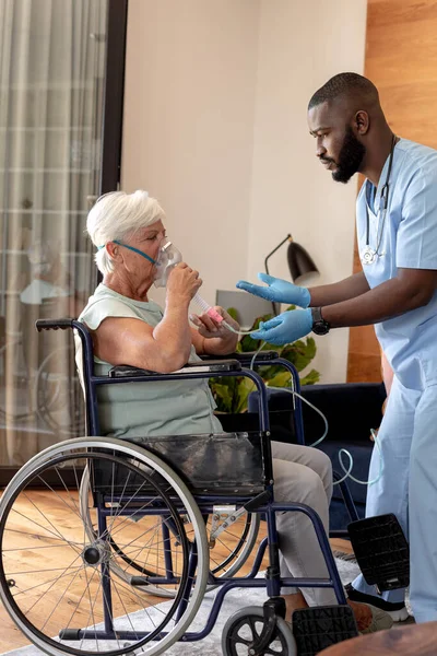 非裔美国男性卫生工作者帮助高加索老年妇女使用氧气面罩 医疗和退休老年人生活方式概念 — 图库照片
