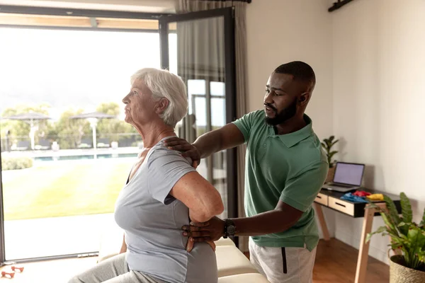 非洲裔美国男性理疗师在家里为高加索老年妇女提供按摩疗法 理疗和康复概念 — 图库照片