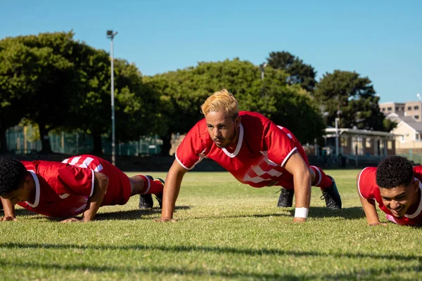 Mužští Multiiraciální Hráči Červených Uniformách Nacvičují Kliky Travnatém Poli Proti — Stock fotografie