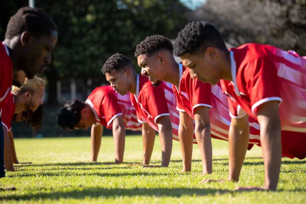 Male Multiracial Players Red Uniforms Practicing Push Ups Row Grassy — Stock Photo, Image