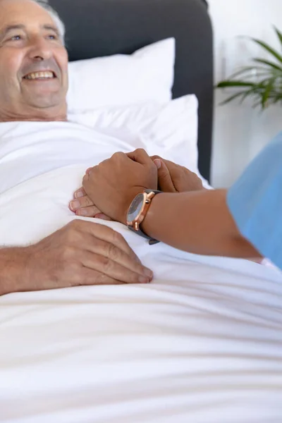 支持高加索老年男子的分娩女性保健工作者的中间部分躺在床上 医疗和退休老年人生活方式概念 — 图库照片