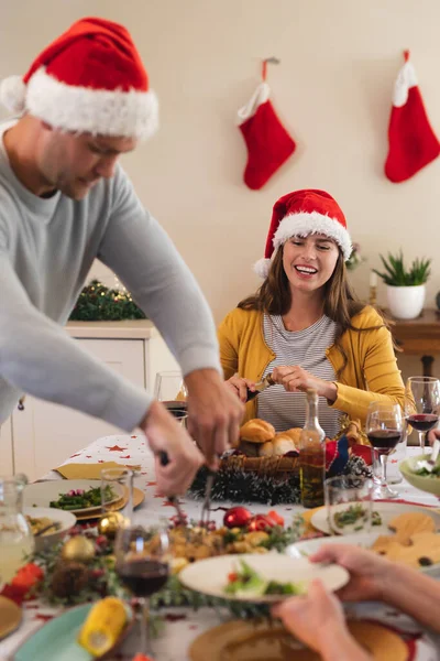 白种人女人坐在餐桌旁吃饭 戴着圣塔帽 面带微笑 优质家庭时间圣诞庆祝活动 — 图库照片