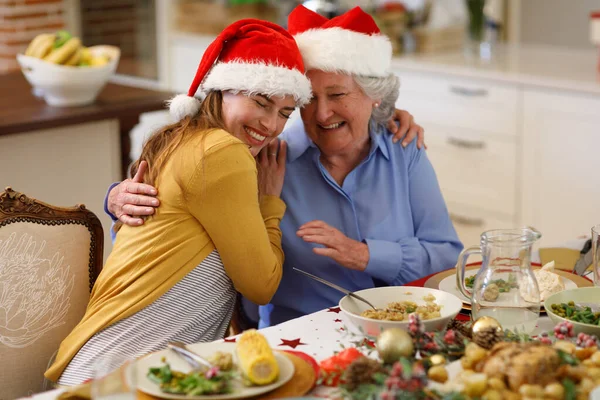 Beyaz Kadın Kıdemli Kadın Masada Oturuyor Kucaklaşıyorlar Noel Baba Şapkaları — Stok fotoğraf