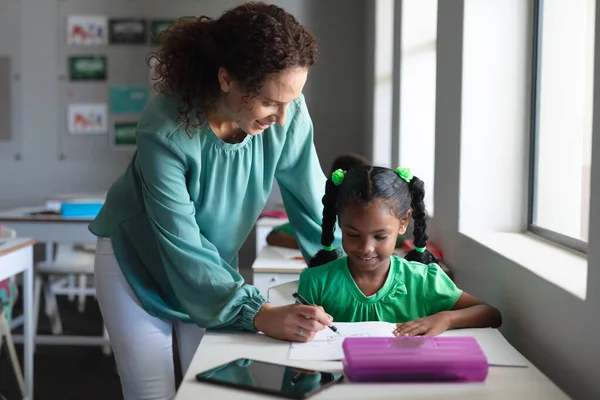 本に書いているアフリカ系アメリカ人の小学生を助ける白人の若い女性教師 変化のない教育子供時代学習職業学校の概念 — ストック写真