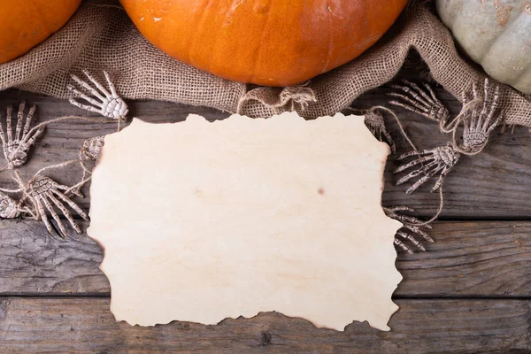 灰色の背景に木製の表面にカボチャや骨格の手に対するコピースペースを持つ紙 ハロウィンのお祭りとお祝いのコンセプト — ストック写真