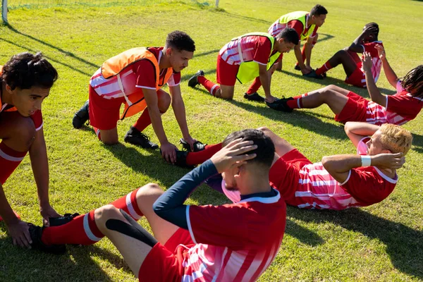 Jogadores Masculinos Multirraciais Segurando Pernas Companheiros Equipe Praticando Crunches Campo — Fotografia de Stock