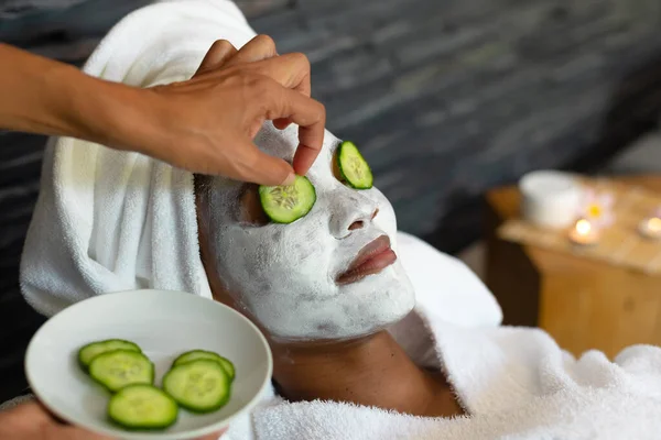 将黄瓜片放在非洲裔美国妇女的眼睛上 她的脸上戴着一副美容美发面具 健康和放松的概念 — 图库照片
