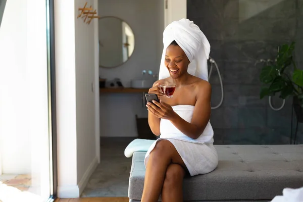Lächelnde Junge Afrikanerin Handtücher Gehüllt Während Sie Mit Dem Smartphone — Stockfoto