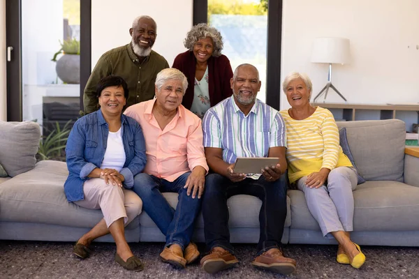 ソファの上で友人とリラックスしてデジタルタブレットを保持幸せな多人種シニア男性の肖像画 老人ホーム 無線技術 変更されていない 生活支援 — ストック写真