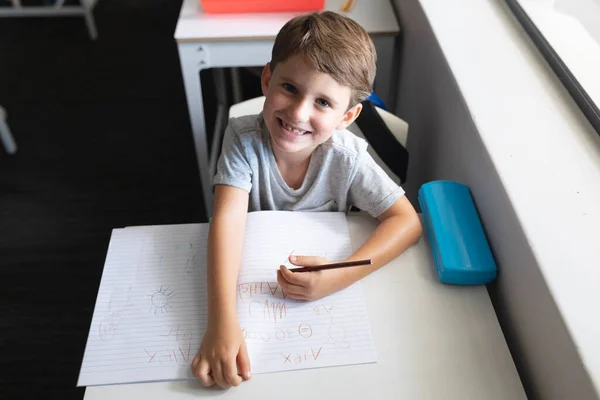 机の上に本とペンで笑顔の白人小学生の高角度肖像画 変化のない教育子供時代学習学校の概念 — ストック写真