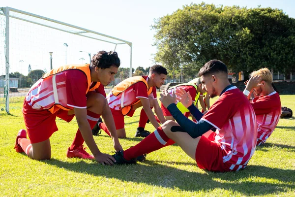 Male Players Holding Legs Multiracial Teammates Practicing Crunches Grassy Field — Stock Photo, Image