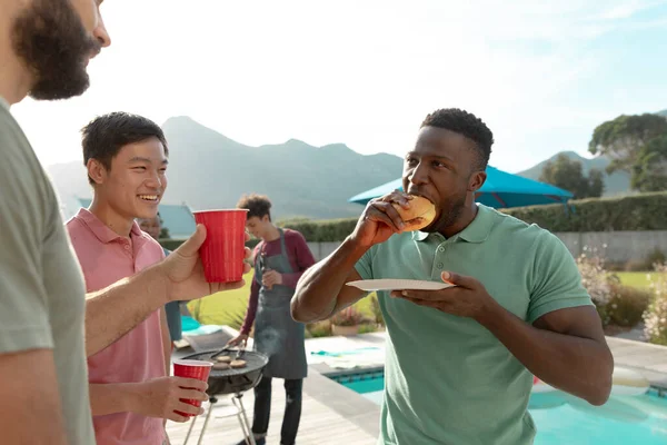 夏天在院子里聚会时 多种族的男性朋友们一边喝啤酒一边吃汉堡包 快乐极了 复制空间 社交活动 娱乐和周末活动 — 图库照片