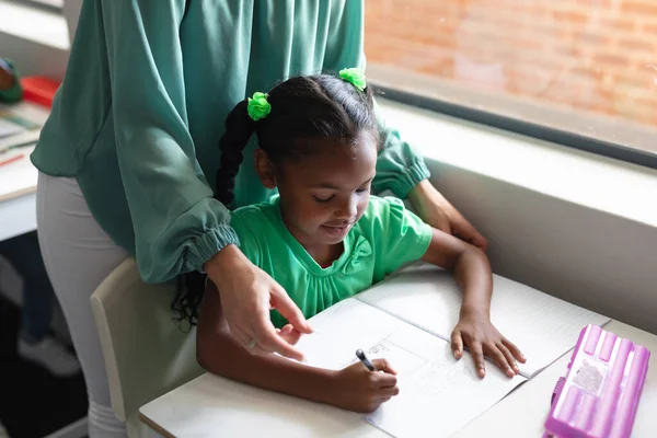 高加索年轻女教师的中段 协助非洲裔美国女学生在课桌前学习 职业和学校概念 — 图库照片
