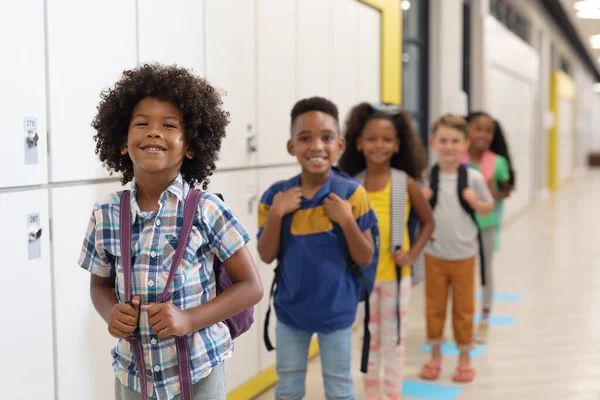 Portret Wielorasowych Uśmiechniętych Dzieci Szkoły Podstawowej Plecakami Stojącymi Rzędzie Niezmienione — Zdjęcie stockowe