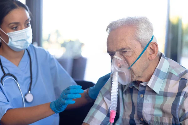 Dwurasowa Pracownica Służby Zdrowia Pomaga Białemu Starszemu Mężczyźnie Używać Maski — Zdjęcie stockowe