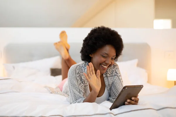 笑着非洲裔美国非洲裔年轻女子一边躺在床上一边挥动着数字平板电脑 一边抄袭空间 生活方式 家庭和技术概念不变 — 图库照片
