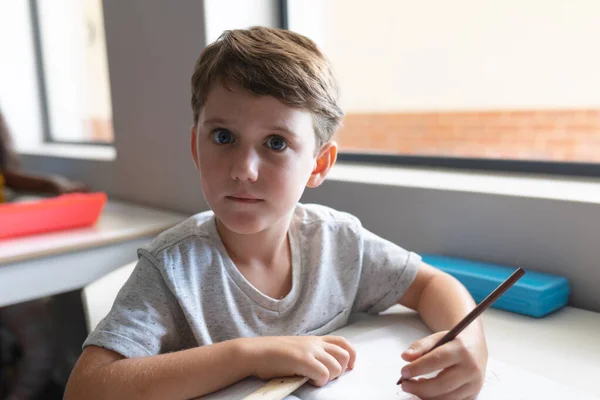 教室の机に座って広い目を持つ白人小学生の肖像画 変化のない教育子供時代学習学校の概念 — ストック写真