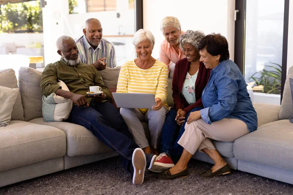 在养老院的沙发上 一位年事已高的妇女与多种族朋友一起使用笔记本电脑 无线技术 辅助生活 退休概念 — 图库照片