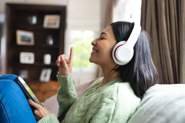 Obraz Szczęśliwej Birasowej Kobiety Słuchawkach Pomocą Smartfona Siedzącego Sofie Domu — Zdjęcie stockowe