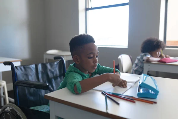 Niño Afroamericano Primaria Escribiendo Libro Mientras Está Sentado Silla Ruedas —  Fotos de Stock