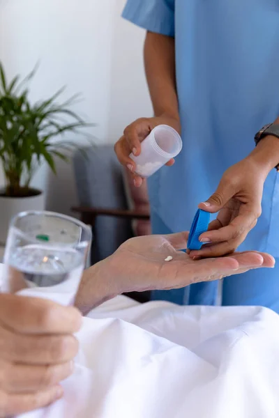 分娩中の女性医療従事者の中央部は ベッドの上で白人のシニア男性に薬を与えます 医療と定年退職シニアライフスタイルの概念 — ストック写真